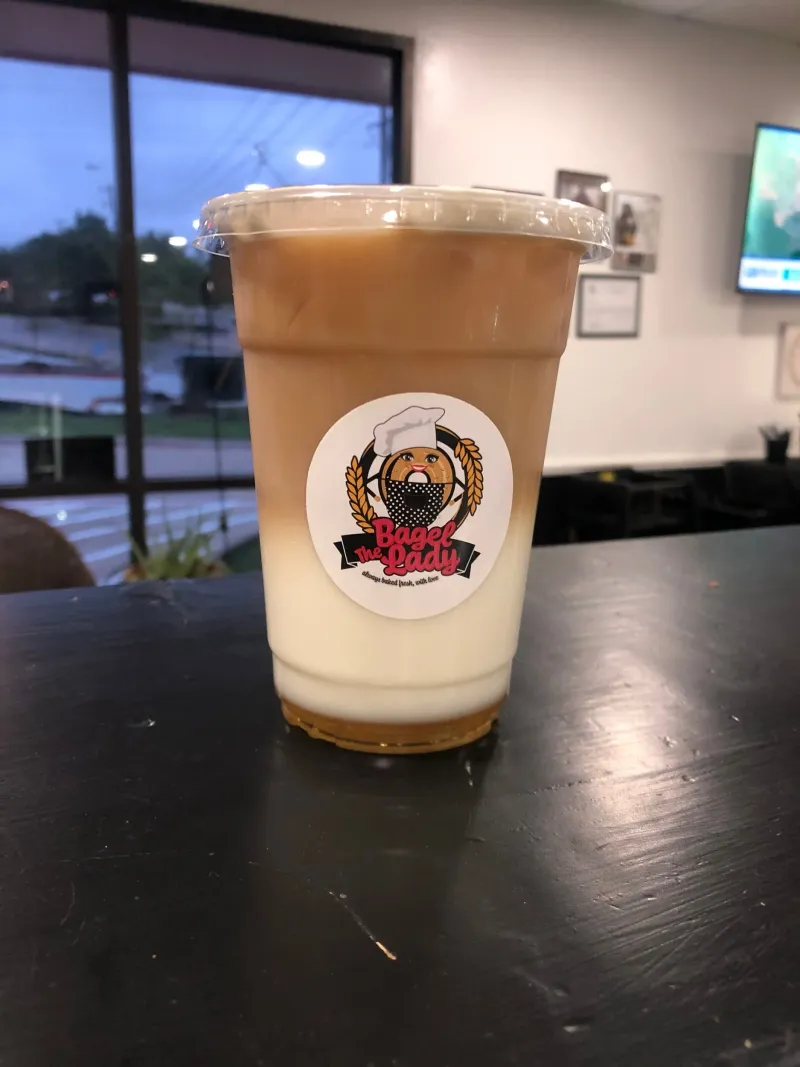 An iced latte with The Bagel Lady logo on the cup