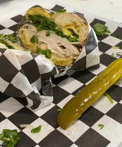 A turkey bagel wrapped in foil with a pickle