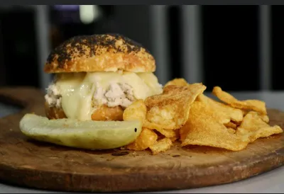 Melted cheese chicken salad bagel with chips and a pickle