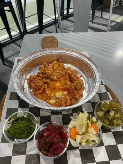 A hot shakshuka pan with pickles and salsa on the side